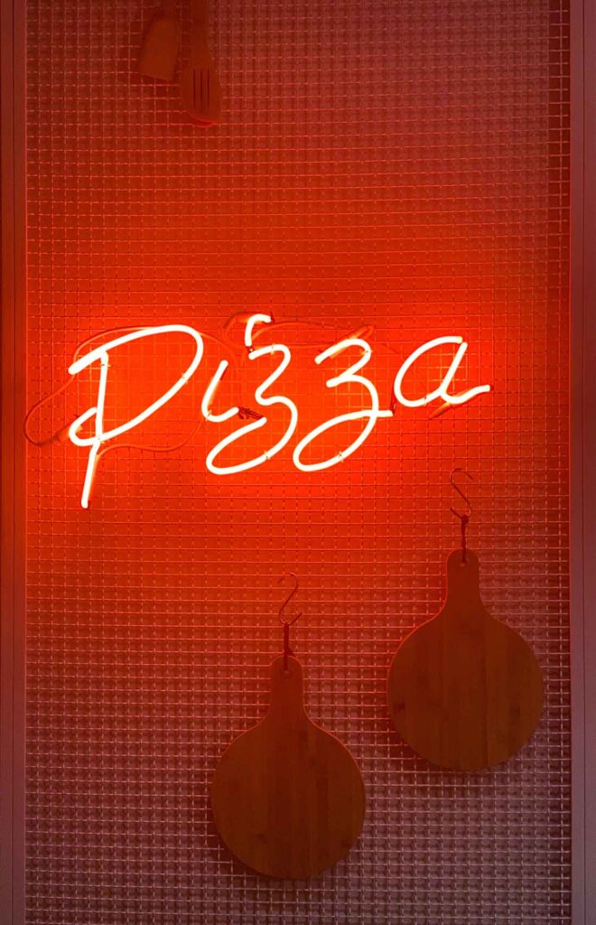 pizza neon sign in red with pizza paddles on the wall