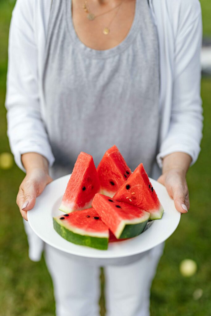 a woman in a white shirt holding a plate of cut up watermelon