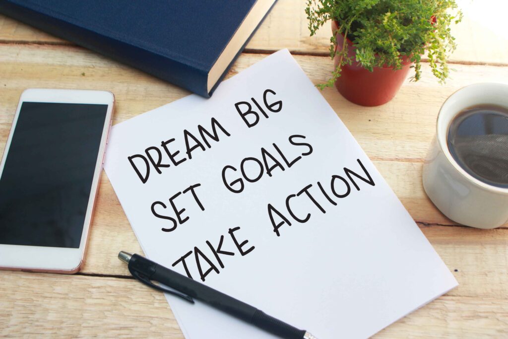 paper with pen on it that says dream big, set goals and take action.  