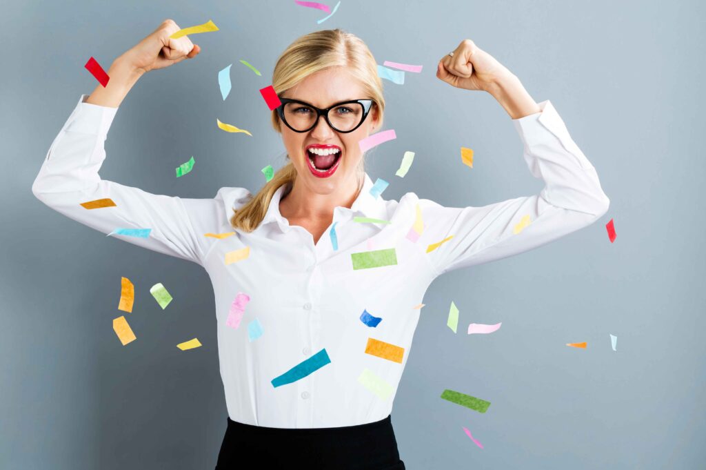 a woman in a white shirt in a celebration stance celebrating with confetti falling - Thrive in business