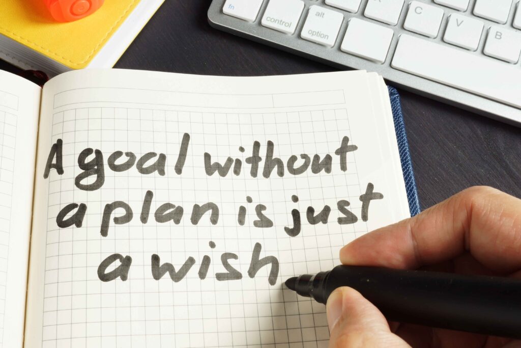 an open notebook with a person writing a goal without a plan is just a wish.  how to stay motiviated as an entrepreneur