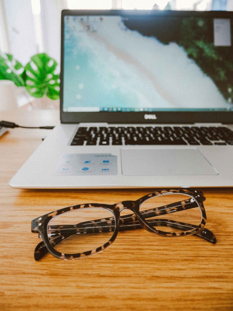 laptop open with glasses sitting on a desk in front of a window - choose a business idea