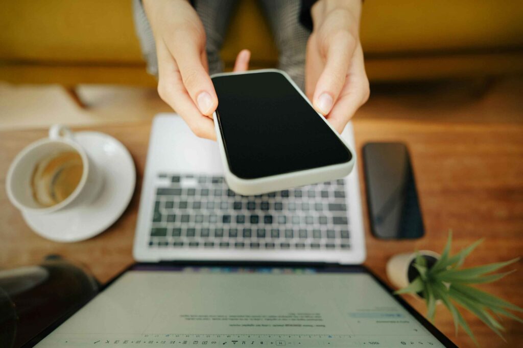 woman holding phone over laptop - hacks to help entrepreneurs thrive