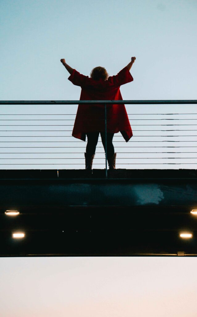 Celebrate the Small Wins as an Entrepreneur. A woman standing on a bridge hands in the air celebrating