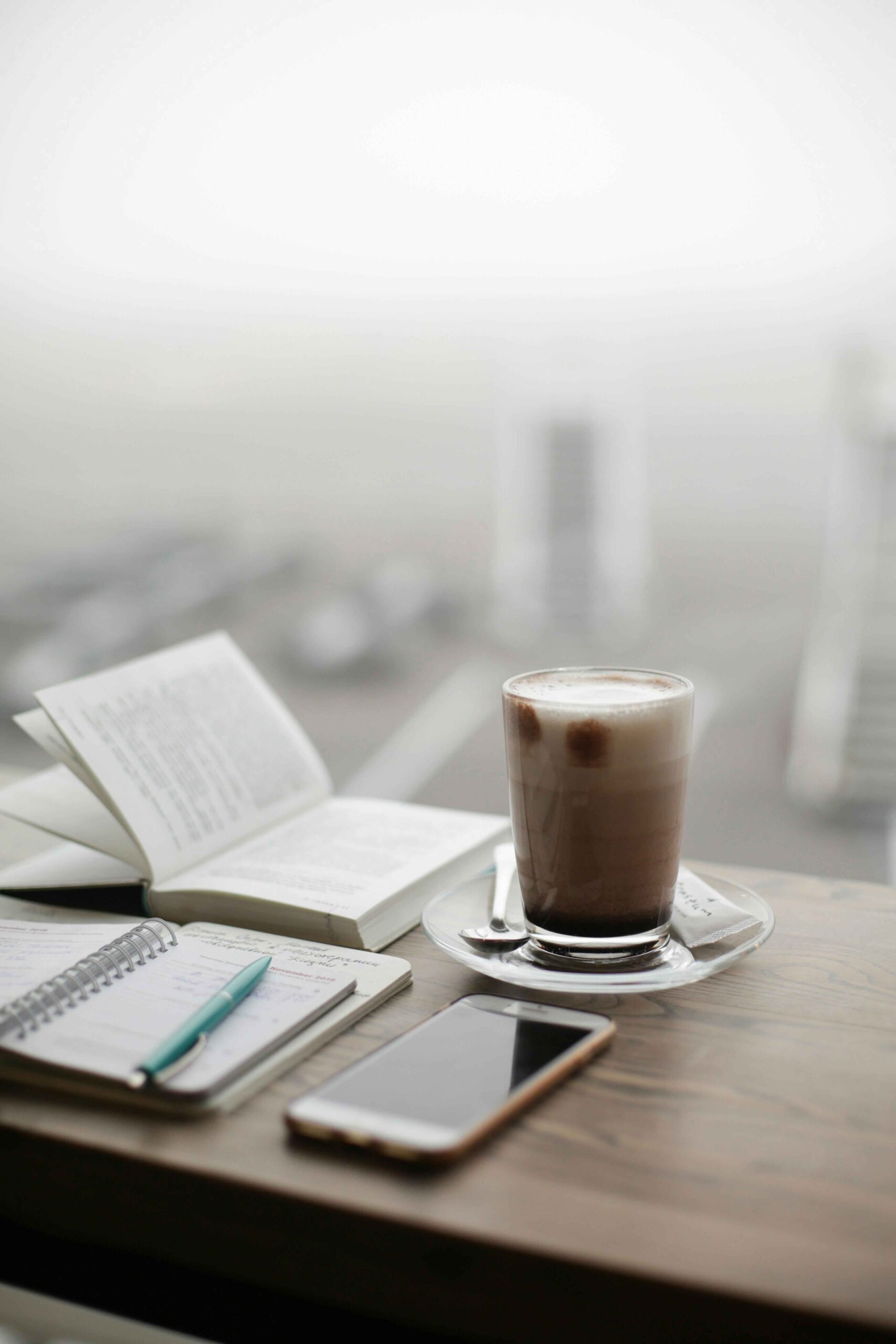 Morning Routine to Supercharge Your Day. cup of coffee on a table in front of a window with a notebook pen and phone